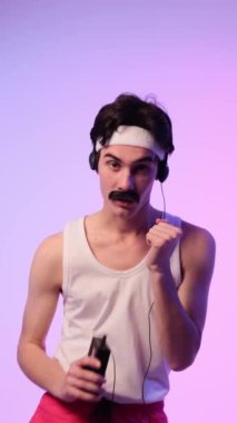 Neşeli Kafkasyalı genç adam 80 'lerin retro kişisel müzik setini kullanarak dans ediyor ve müzik dinliyor, mor arka planda duruyor. Dikey video.