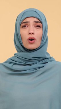 Bej arka planda duran tesettürlü mutsuz bir Arap genç kadının portresi. Duygusal stres ve hayal kırıklığı kavramı. Dikey video.