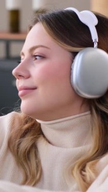 Neşeli, genç, beyaz bir kadın evde kulaklıkla müzik dinliyor. Boş zaman ve zevk kavramı. Dikey video.