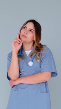 Kafası karışmış kadın tıp doktoru mavi arka planda seçim yapıyor ve sorunu çözüyor. Hayal gücü ve tefekkür kavramı. Dikey video.