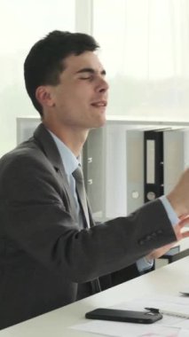 Modern ofiste müzik eşliğinde dans eden, şarkı söyleyen ve iş gününün tadını çıkaran mutlu beyaz bir erkek. Dikey video.