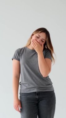 Uykusuz ya da tembel beyaz kadın esniyor ve esniyor, beyaz arka planda duruyor. Yorgunluk, yorgunluk ve yorgunluk konsepti. Dikey video.