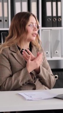 Belgelerle çalışan ve ofiste video görüşmeleri yapan Kafkasyalı genç, yetişkin bir kadın serbest çalışan. Çevrimiçi toplantı ya da Webinar konsepti. Dikey video.