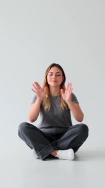 Nilüfer pozisyonunda meditasyon yapan sakin bir kadın yoga sırasında beyaz arka planda. Refah ve zen kavramı. Dikey video.