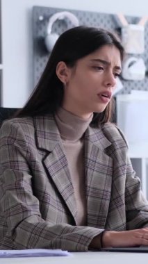 Ofiste dizüstü bilgisayarla çalışırken kafası karışmış genç beyaz kadın çalışanın yüz hareketi. Dikey video.