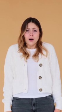 Korkak genç beyaz kadın bej arka planda duran yüzü örtüyor. Korku, korku ve korku kavramı. Dikey video.