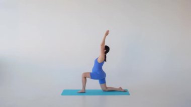 Orta yaşlı, Kafkasyalı hamile kadın sporcu hamleler sırasında esneyip nefes alıyor, beyaz arka planda bebek eğitimi alıyor..