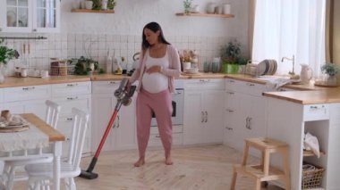 Hamile, gülümseyen, orta yaşlı, orta yaşlı bir kadın evde temizlik ve mutfak zeminini süpürüyor. Ev temizliği ve ev temizliği kavramı.
