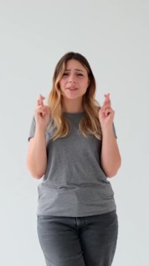 Beyaz arka planda duran neşeli, genç, beyaz, beyaz bir kadın. İnancın, servetin ve hayalin işareti. Dikey video.