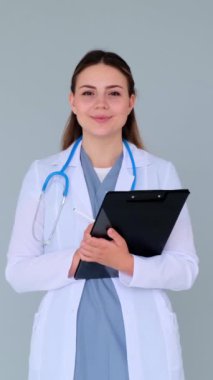 Dost canlısı ve misafirperver genç, beyaz, mavi arka planda tıbbi pratisyen bir kadının portresi. Pozitif doktor ya da hemşire. Dikey video.