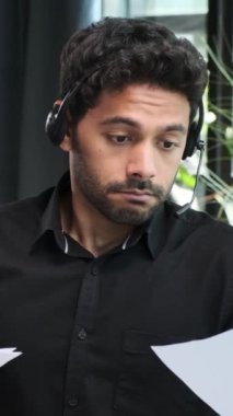 Konsantre olmuş Ortadoğu erkek çevrimiçi destek yöneticisi müşteriyle uzaktan görüşüyor ve ofiste belgelerle çalışıyor. Dikey video.