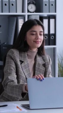 Neşeli Kafkasyalı genç yetişkin iş kadını iş gününü sonlandırıyor, masa başında sipariş veriyor ve hafta sonu veya tatilde ofiste çalışmaya hazırlanıyor. Dikey video.