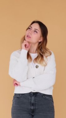 Heyecanlı genç beyaz kadın çözüm arıyor ve bej arka plan konusunda parlak fikirleri var. Beyin fırtınası, istihbarat konsepti. Dikey video.