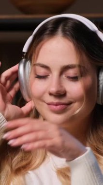 Mutlu ve dingin genç beyaz kadın gece yarısı evde, kulaklık takıp kanepede dinleniyor. Dikey video.