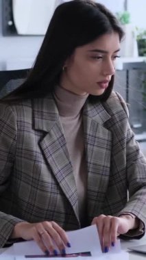 Gergin kadın Kafkasyalı ofis çalışanı, kağıtlarla çalışıyor, ofiste masa başında oturuyor. Panik, stres, zorluk kavramı. Dikey video.