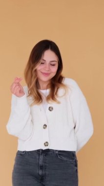 Kafkasyalı genç bir kadın kalp şeklinde flört ediyor, bej arka planda duruyor. Sevgi ve sevginin sembolü. Dikey video.