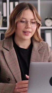 Çevrimiçi eğitim veren ya da ofiste dizüstü bilgisayarla çalışan genç, beyaz bir iş kadını. Video görüşmesi kavramı. Dikey video.