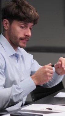 Ofiste gazetelerle çalışırken kahve içen orta yaşlı beyaz bir işadamı. Yorgunluk kavramı. Dikey video.