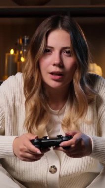 Konsantre olmuş Kafkasyalı genç kadın oyun sahası kullanarak video oyunu oynuyor ve gece yarısı evinde yenilgiye uğruyor. Dikey video.