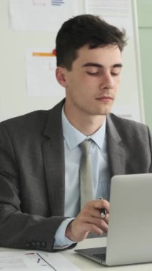 Modern ofiste dizüstü bilgisayarla çalışırken neşeli, genç, beyaz iş adamı dans edip şarkı söylüyor. Dikey video.