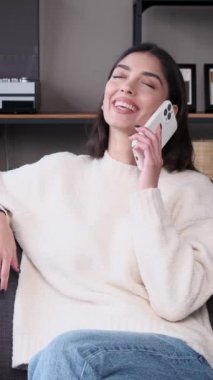 Neşeli, beyaz, yetişkin bir kadın cep telefonuyla hafta sonunu evde geçiriyor. Uzaktan konuşma ya da tartışma kavramı. Dikey video.