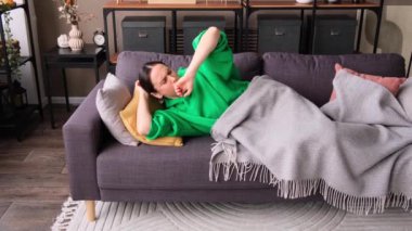 Yorgun ve yorgun orta yaşlı beyaz kadın gündüz uyanıp evdeki kanepede rüya görüyor, boş vakitlerini geçiriyor. Tembellik kavramı.