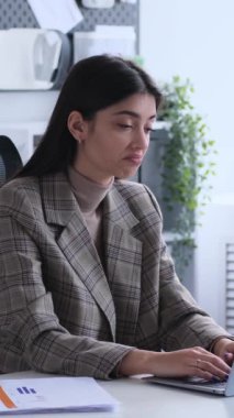 Kafası karışmış beyaz kadın çalışan modern ofiste dizüstü bilgisayarla çalışırken omuz silkiyor. Dikey video.