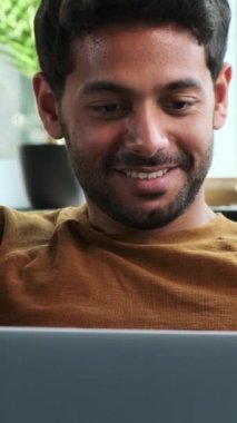 Dost canlısı bir Orta Doğulu genç adamın portresi. Evdeki sanal dünyada sohbet etmek için dizüstü bilgisayar kullanıyor. Sosyal medyada mesajlaşma kavramı. Dikey video.