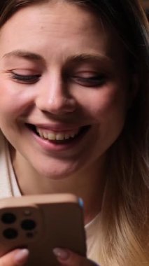 Kafkasyalı genç bir kadının sosyal medyada boş zamanlarını cep telefonuyla geçirip akşam evde gülüşünü yakından çek. Dikey video.