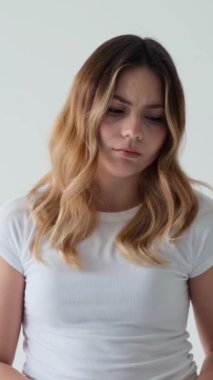 Beyaz arka planda umutsuzluk ve keder içindeki Kafkasyalı genç bir kadın. Hayal kırıklığı, stres ve üzüntü kavramı. Dikey video.