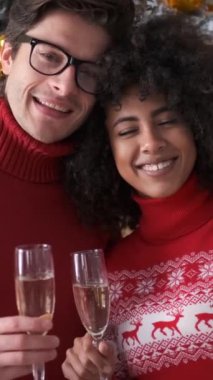 Mutlu genç çift Noel ağacının önünde şampanya bardakları tutuyor.