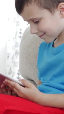 Smiley Kafkasyalı küçük çocuk evde tabletle çevrimiçi eğlence yapıyor. İnternette dijital bir eğlence kavramı. Dikey video.