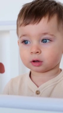 Evinde beşikte oynayan sevimli ve pozitif beyaz bir çocuğun portresi. Çocukluk ve masumiyet kavramı. Dikey video.