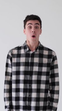 Şaşırmış ve şaşırmış beyaz arka planda dikildiğini haykıran beyaz bir genç adam. Ödül, zafer ve başarı kavramı. Dikey video.