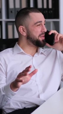 Ofiste telefon görüşmeleri sırasında neşeli orta yaşlı beyaz bir erkek müşteriyle sohbet ediyor. Profesyonel müzakere kavramı. Dikey video.