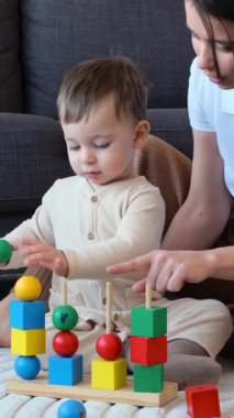 Neşeli, genç, beyaz bir anne ve bebek birlikte oturma odasında oynuyorlar. Boş zaman, eğitim ve eğlence konsepti. Dikey video.