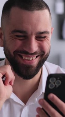 Ofiste çalışırken çevrimiçi hobi olarak cep telefonu kullanan orta yaşlı, mutlu bir beyaz erkek. Boş zaman ve rahatlama kavramı. Dikey video.