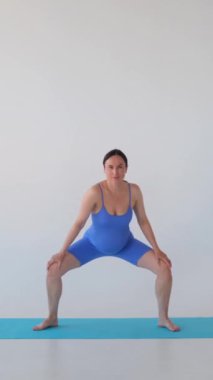 Pozitif orta yaşlı beyaz hamile kadın omuzlarını esnetiyor, spor yapıyor ya da beyaz arka planda egzersiz yapıyor. Dikey video.