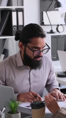 Odaklanmış ve konsantre olmuş iş arkadaşları birlikte brifing veriyorlar, büroda evrak işleri ve iş stratejileri planlıyorlar. Dikey video.
