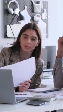 Modern ofiste toplanırken bilgisayar ve mali belgelerle birlikte çalışan düşünceli çok uluslu iş arkadaşları. Dikey video.