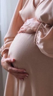 Hamile, beyaz bir kadının evdeki bir tümseğin üzerinden parmak fırçalarken yakın çekim görüntüsü. Kadınlık, heyecan ve annelik kavramı. Dikey video.