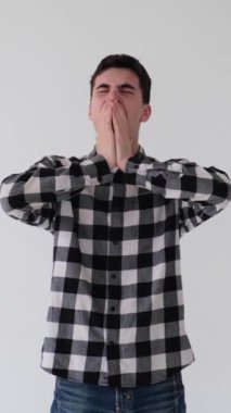 Uykulu ve tembel beyaz bir gencin portresi esniyor, beyaz arka planda duruyor. Yorgunluk ve yorgunluk kavramı. Dikey video.