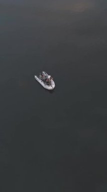 Tatilin tadını çıkaran iki adamın akşam etrafı doğa ile çevrili sakin bir gölde tekneden çubuklarla balık tutarken çekilmiş görüntüleri. Dikey video.