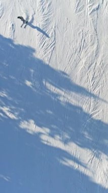 Karlı bir kayak pistindeki kayakçıların hava görüntüleri. Etrafı resimli bir kış manzarasıyla çevrili. Açık hava eğlencesi ve doğa harikası. Dikey video.