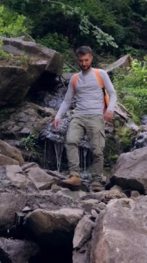 Zengin bir ormandaki şelalenin yakınındaki kayalık araziyi doğa yürüyüşü sırasında gezen ve keşfeden bir adam maceraperest ve manzaralı bir doğa deneyimi yaşıyor. Dikey video.