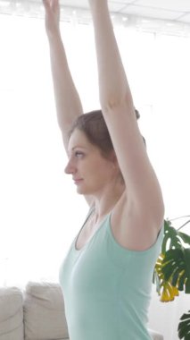 Kafkasyalı orta yaşlı kadın Asya dansı yapıyor ya da evde yoga yaparken egzersiz yapıyor. Refah ve sükunet kavramı. Dikey video.