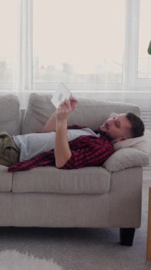 Neşeli Kafkasyalı orta yaşlı adam evde boş zaman geçirmek için online eğlence için tablet kullanıyor. Zevk kavramı ve rahatlama. Dikey video.