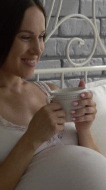 Hamile kadın yatakta dinleniyor, evde dizüstü bilgisayarından film izliyor. Kendi evinde huzurlu ve keyifli bir anın tadını çıkarırken, mutluluk ve rahatlık. Dikey video.