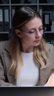 Akşam ofisinde çalışan, evrak işleriyle ve strateji planlamalarıyla uğraşan, ciddi, genç, beyaz bir iş kadını. Dikey video.