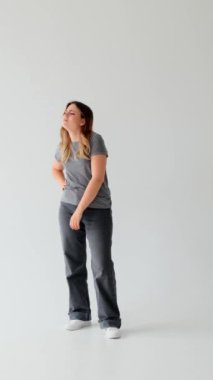 Beyaz arka planda sıkıntıdan ve ilgisizlikten muzdarip beyaz bir genç kadın. Melankoli, yalnızlık ve yorgunluk kavramı. Dikey video.